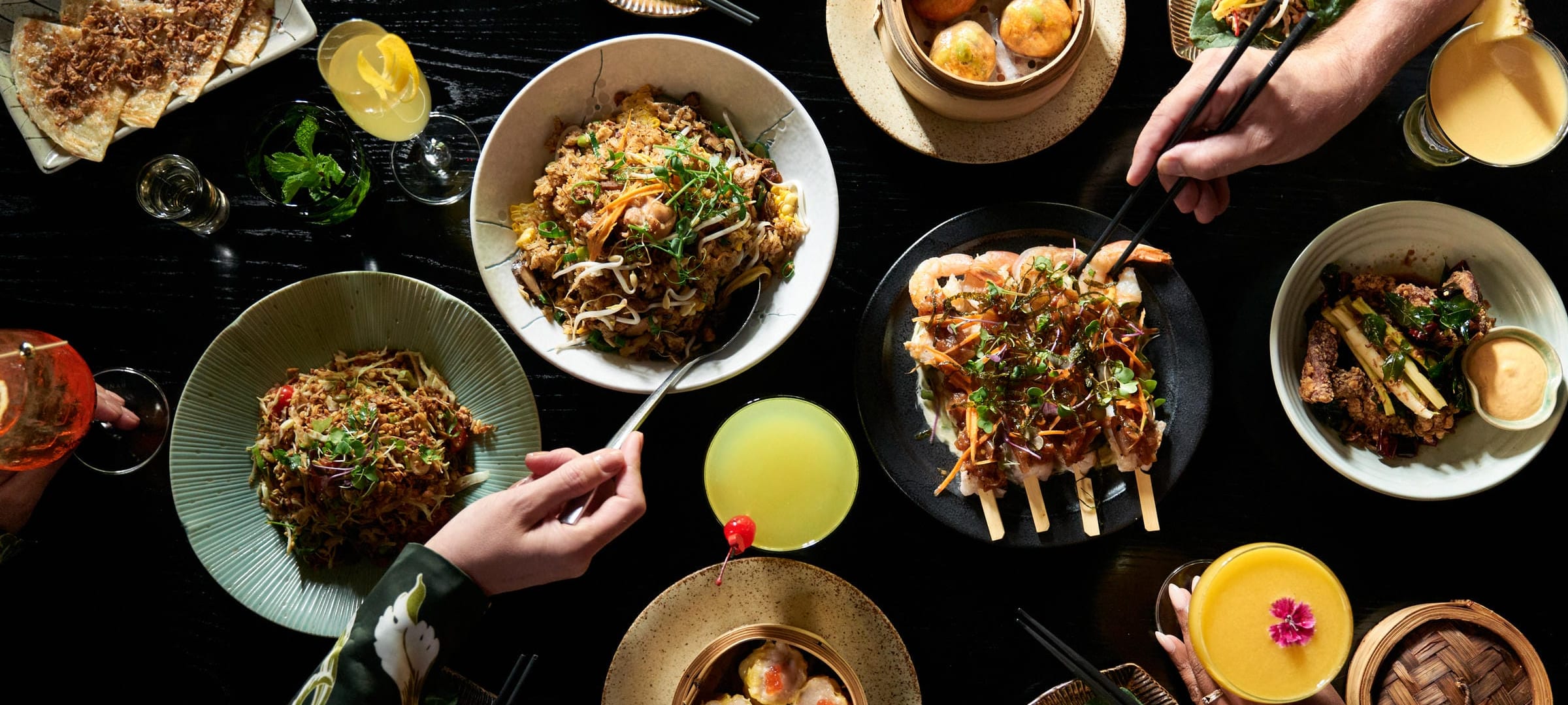 Friends sharing dinner at Zodiac, chopsticks reaching across noodles, skewers and dumplings